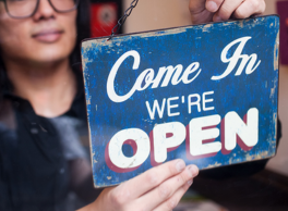 Business owner at a window holding a sign saying "Come In. We're Open"