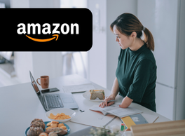 A woman missing her left forearm works on her laptop at her kitchen island next to an Amazon logo.