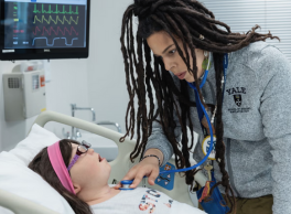Yale nurse using a stethoscope on a manikin representing a female patient with down syndrome.
